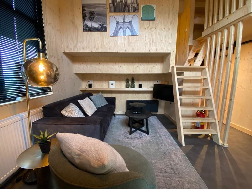 Ruime woonkamer met houten wanden, een bank, tv-kast, trap naar een bovenverdieping en een moderne lamp