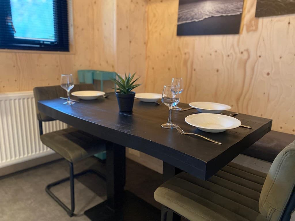 Eettafel met vier borden en glazen in een houten omgeving, groene stoelen en kunst aan de muur.