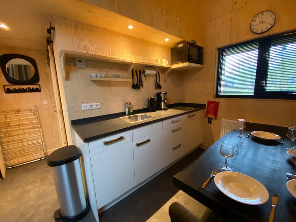 Moderne keuken met houten wanden, aanrecht, magnetron, en eettafel met servies in EuroParcs Resort De Utrechtse Heuvelrug.