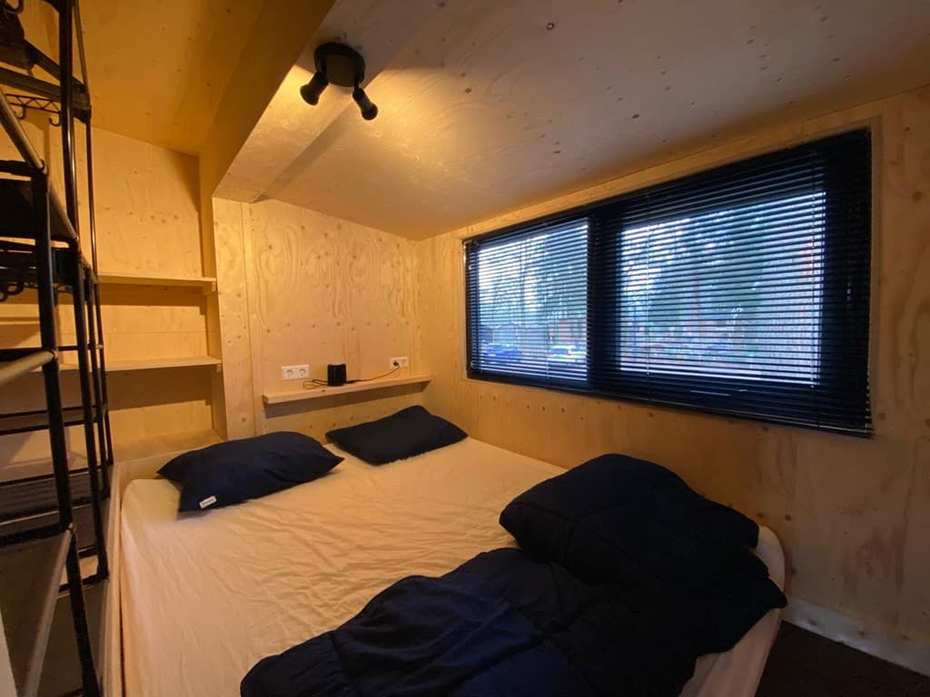 Sfeervolle slaapkamer met een tweepersoonsbed en een grote raampartij met zwarte jaloezieën.