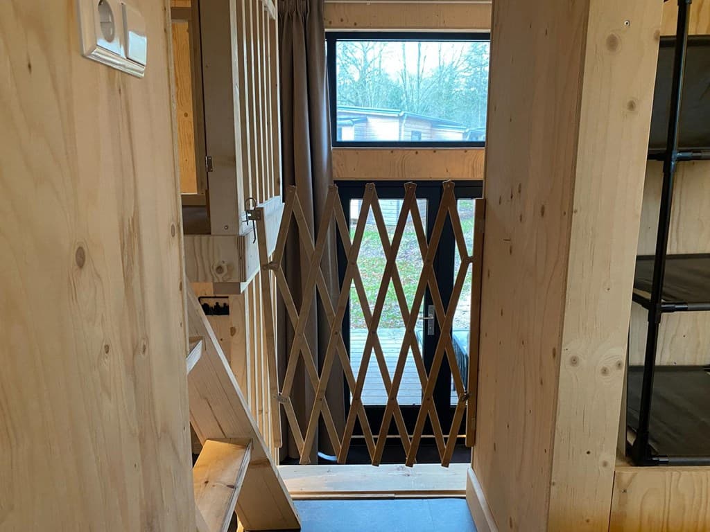 Ingang van een woning met een houten hekje, trappen en grote ramen met uitzicht op groen.