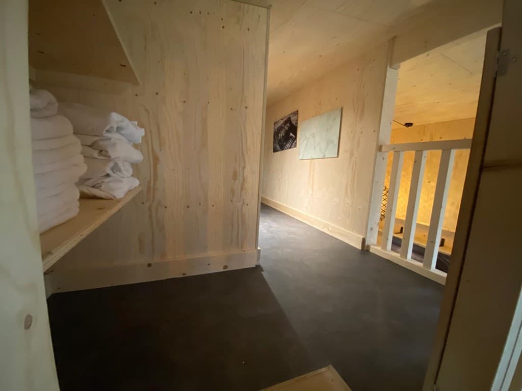 Houten interieur van een woning met een slaapkamer en ruimte voor handdoeken op een plank.
