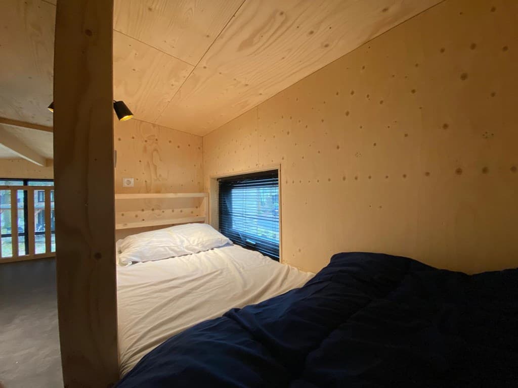 Slaapgedeelte met een tweepersoonsbed, houten wanden en een raam met verduistering in een vakantiewoning.