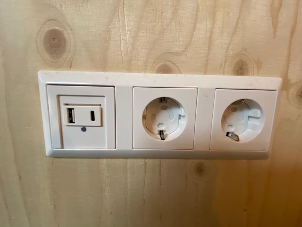 Wand met drie stopcontacten, waaronder één USB-oplaadpunt, tegen een houten achtergrond.