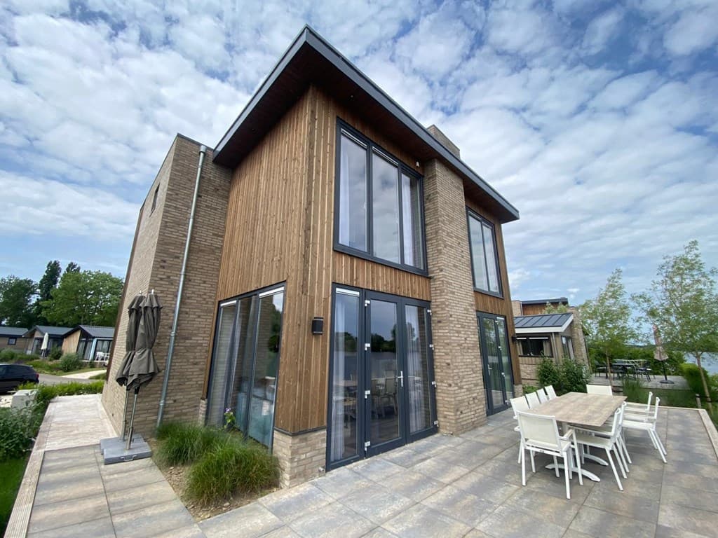 Moderne vakantiewoning met houten gevel, grote ramen en een terras met tafel en stoelen aan een rustige straat