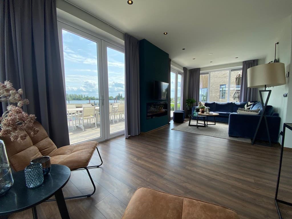 Licht en modern interieur met grote ramen, loungeset en eettafel met uitzicht op het water.