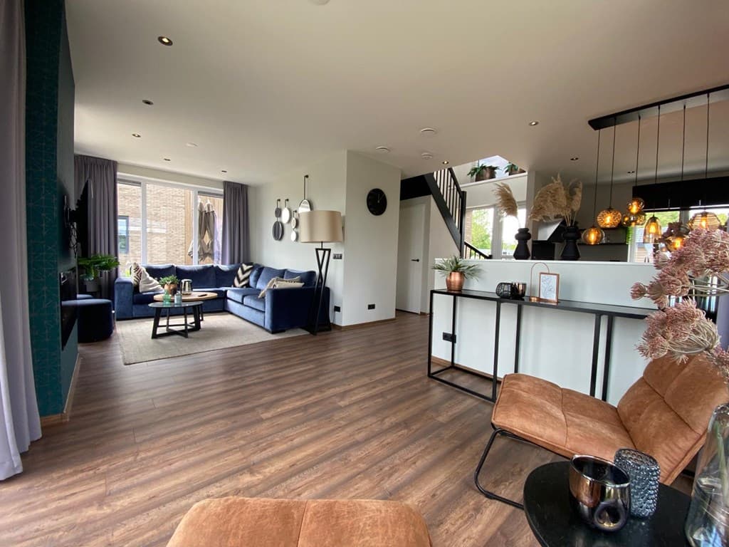 Moderne woonkamer met bank, tv, en open keuken, grote ramen en stijlvolle inrichting met planten en decoratieve elementen