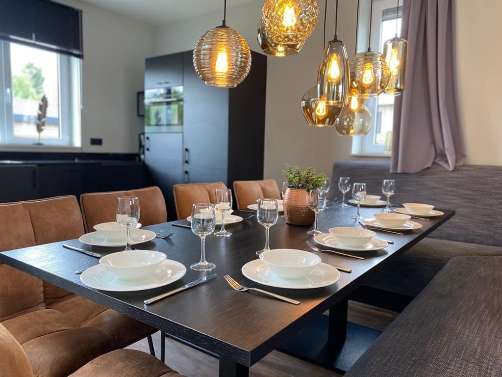 Eetkamer met een grote tafel, acht borden en glazen, verlichte hanglampen en moderne inrichting.