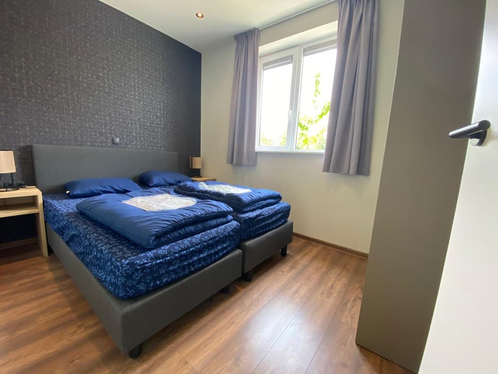 Slaapkamer met twee losse bedden, gordijnen en een raam met uitzicht op de buitenruimte, houten vloer en nachtkastjes