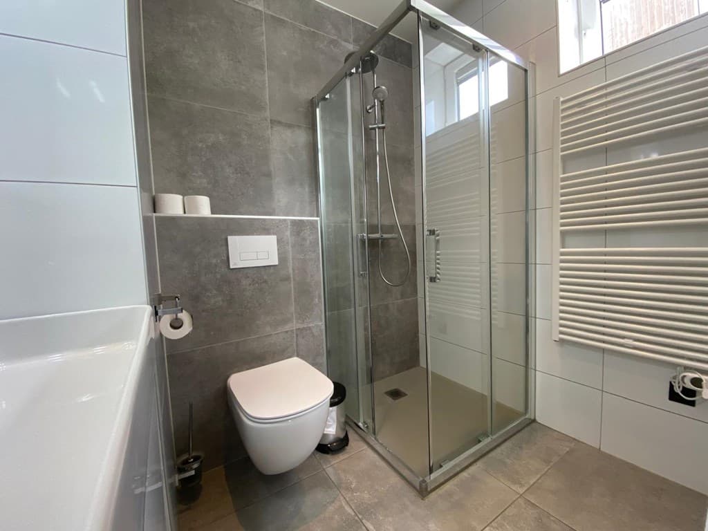 Moderne badkamer met inloopdouche, toilet en handdoekradiator in neutrale kleurstelling.