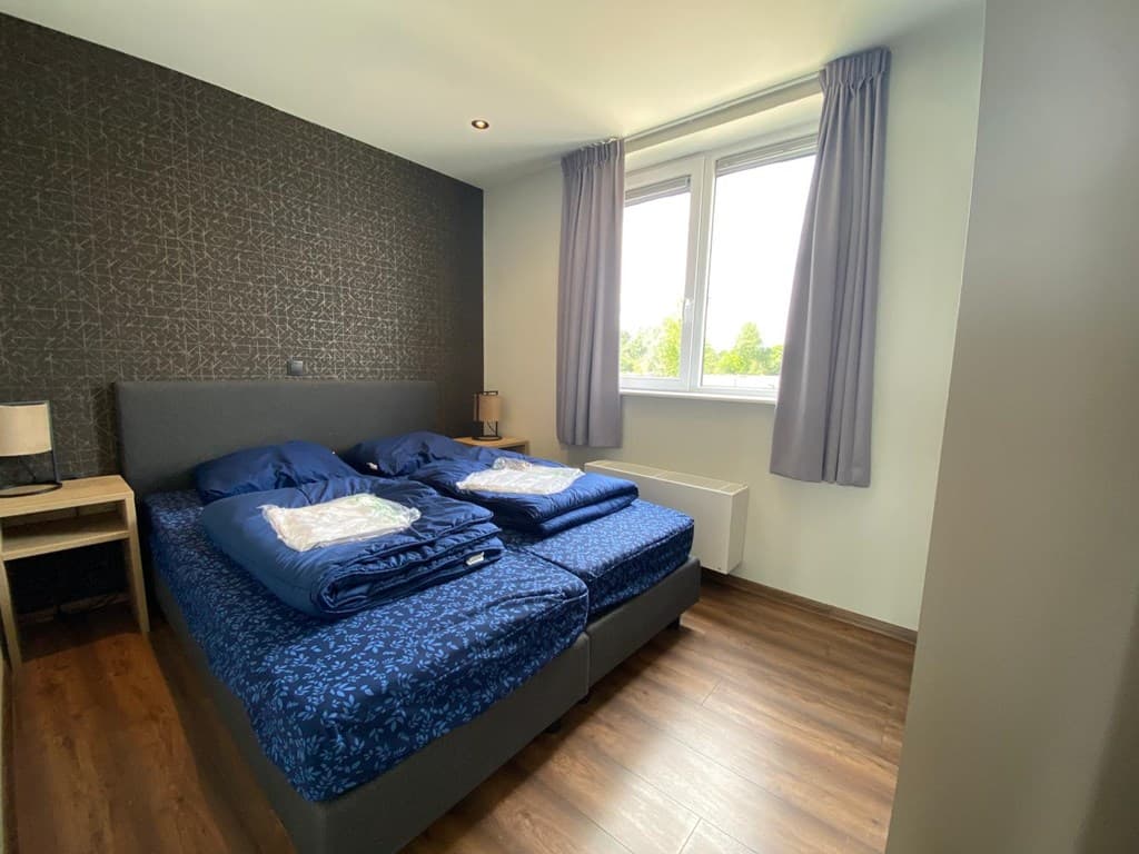 Slaapkamer met twee eenpersoonsbedden, raam met gordijnen en laminaatvloer.