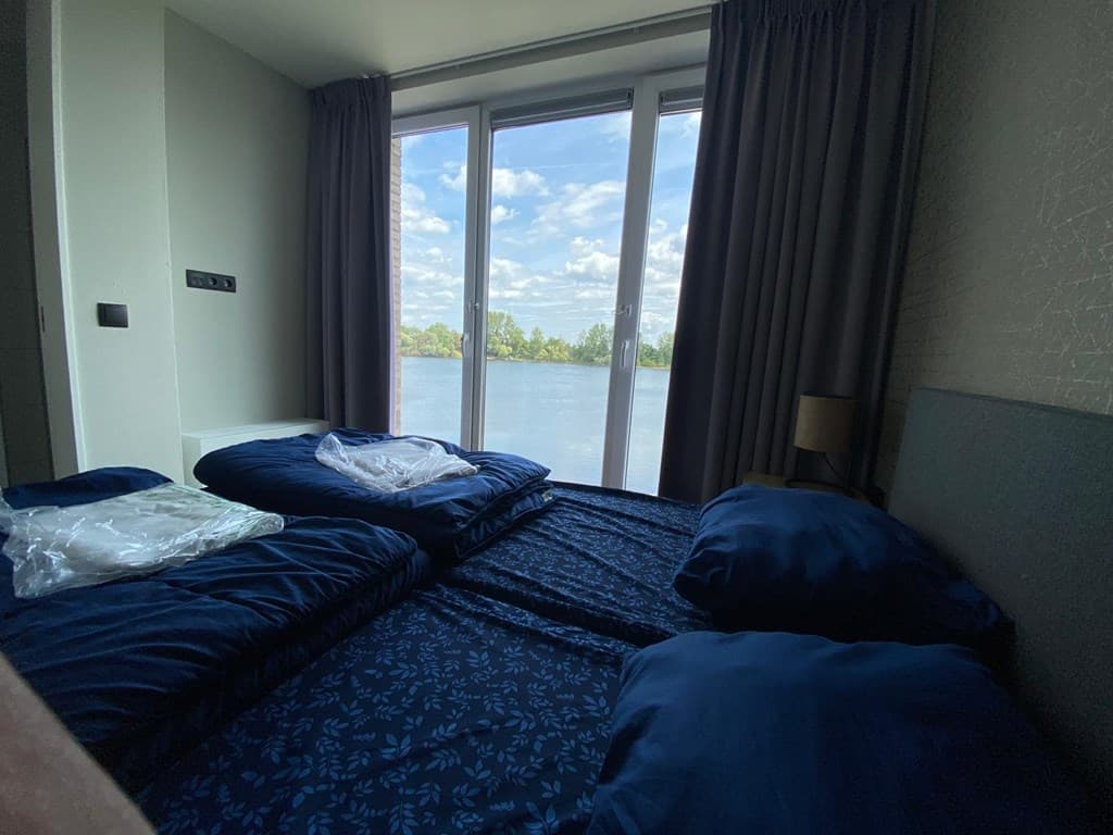 Slaapkamer met twee eenpersoonsbedden en grote ramen met uitzicht op het water en de natuur buiten