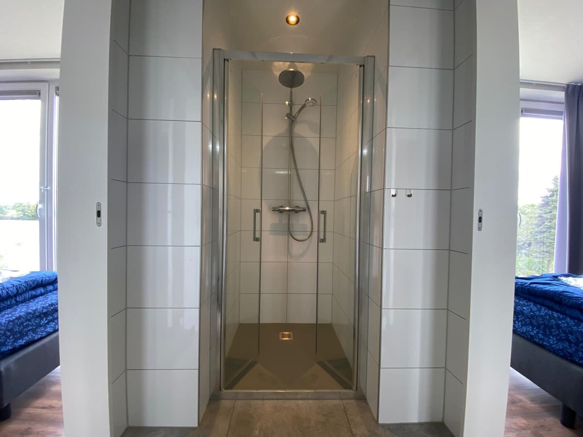 Inloopdouche met moderne tegels en glasdeur in een lichte badkamer met uitzicht naar buiten.