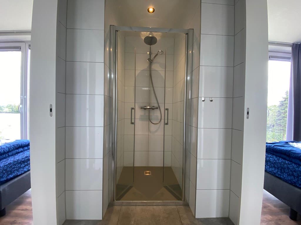 Inloopdouche met moderne tegels en glasdeur in een lichte badkamer met uitzicht naar buiten.