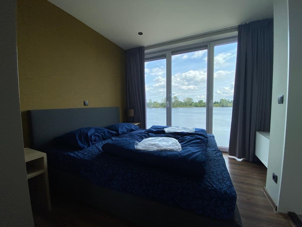 Sfeervolle slaapkamer met tweepersoonsbed en uitzicht op het water door grote glazen schuifdeuren