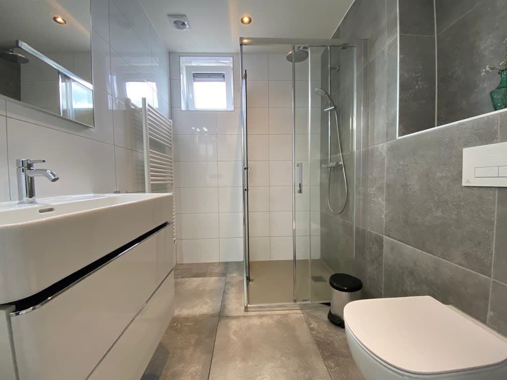 Moderne badkamer met inloopdouche, toilet, wastafel en betegelde muren in grijstinten
