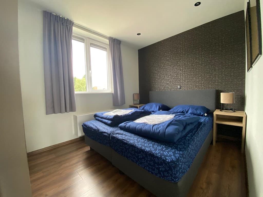 Slaapkamer met twee bedden, gordijnen, een nachtkastje en een raam met uitzicht naar buiten