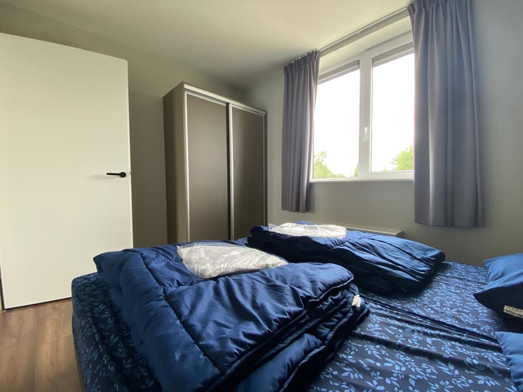 Slaapkamer met een bed, dekbedden, kasten en een raam met uitzicht op de buitenruimte