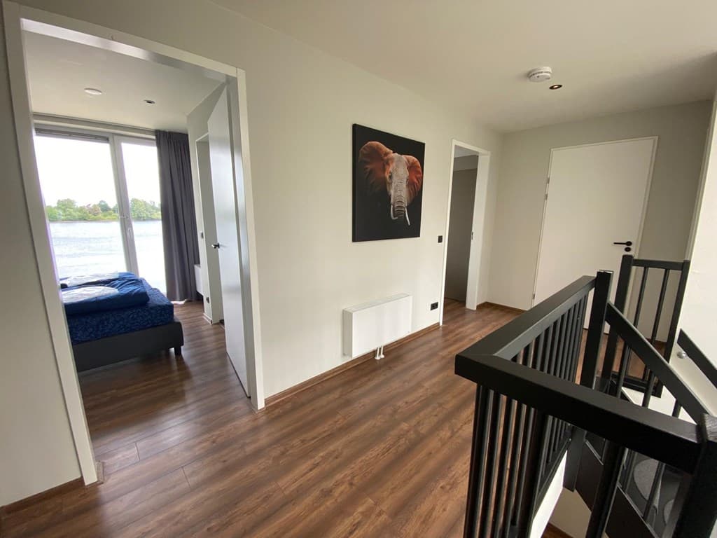 Hal met houten vloer, deuren naar slaapkamers en een schilderij van een olifant aan de muur met uitzicht op water.