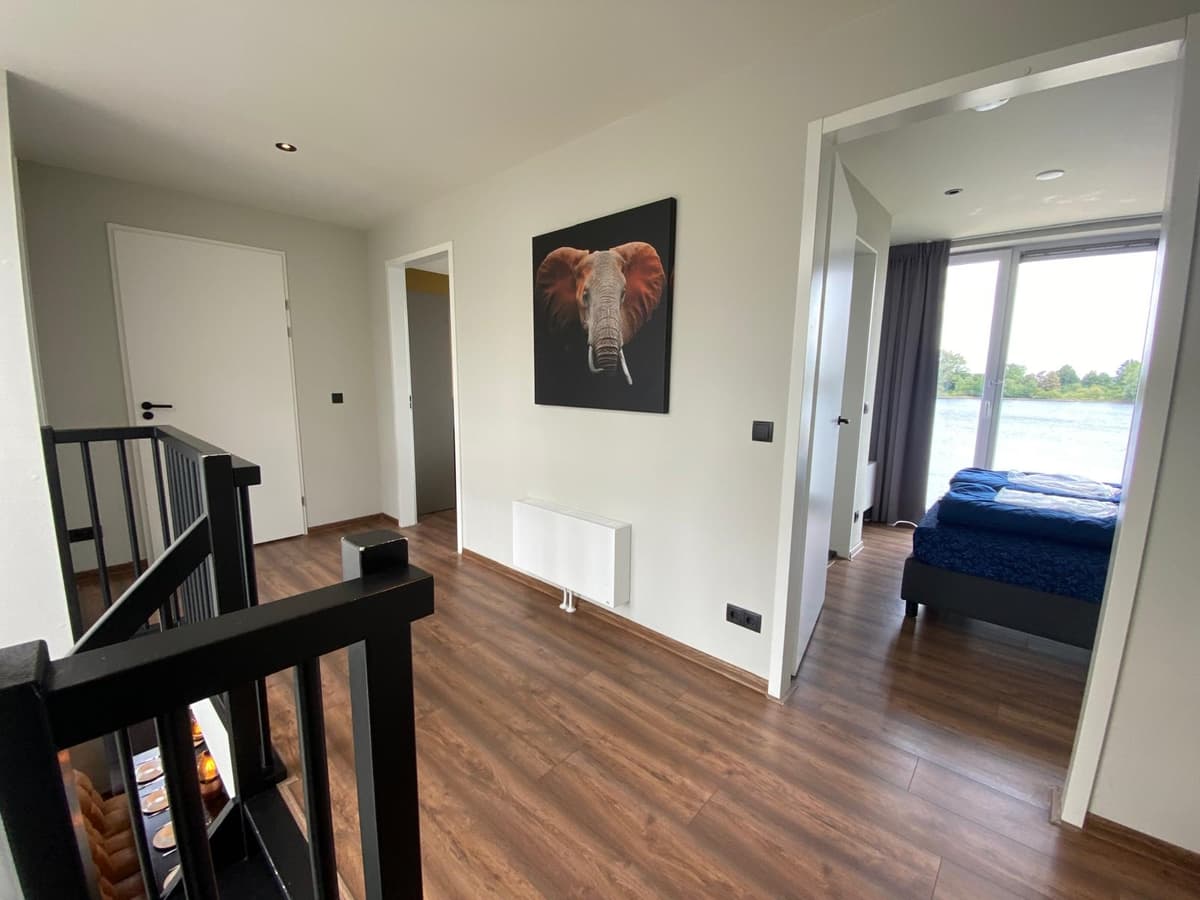 Licht interieur met houten vloer, kunstwerk van een olifant aan de muur en toegang tot een slaapkamer met uitzicht op de Maas