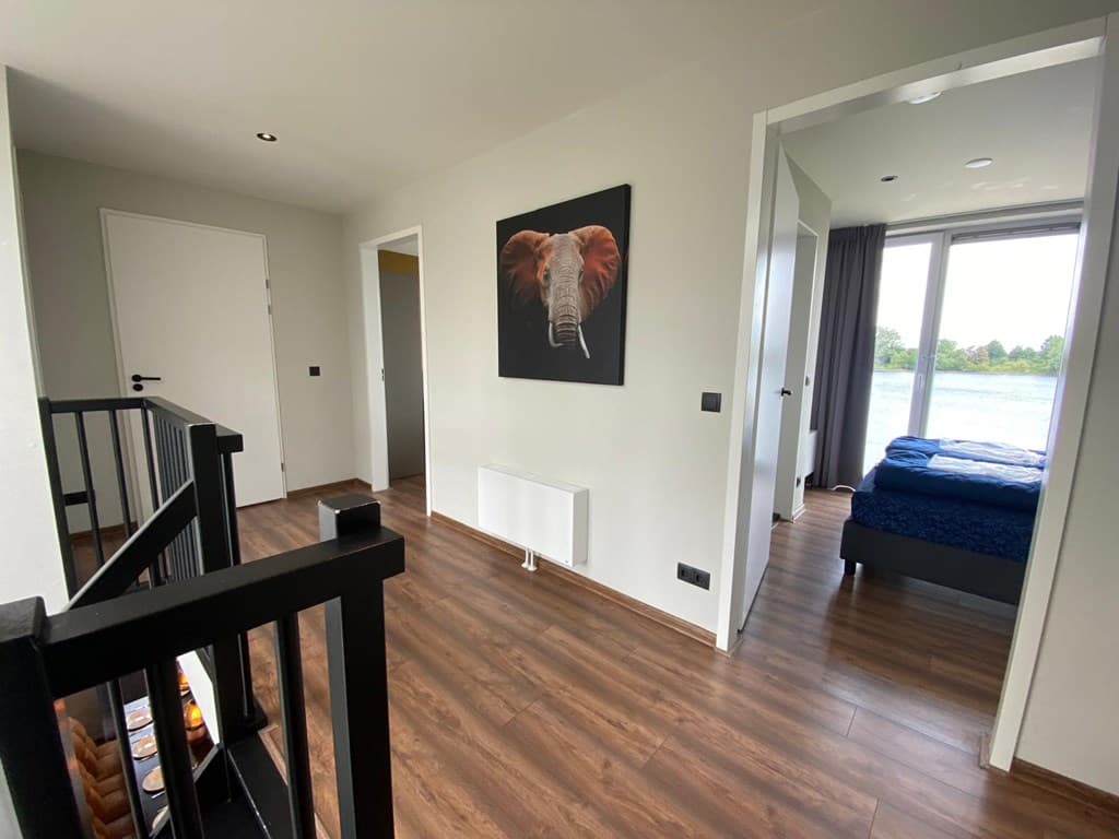Licht interieur met houten vloer, kunstwerk van een olifant aan de muur en toegang tot een slaapkamer met uitzicht op de Maas