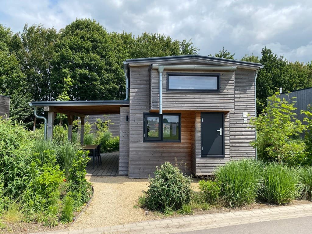 Houten vakantiehuis met ruime veranda, omgeven door groene planten en bomen in EuroParcs Marina Strandbad.