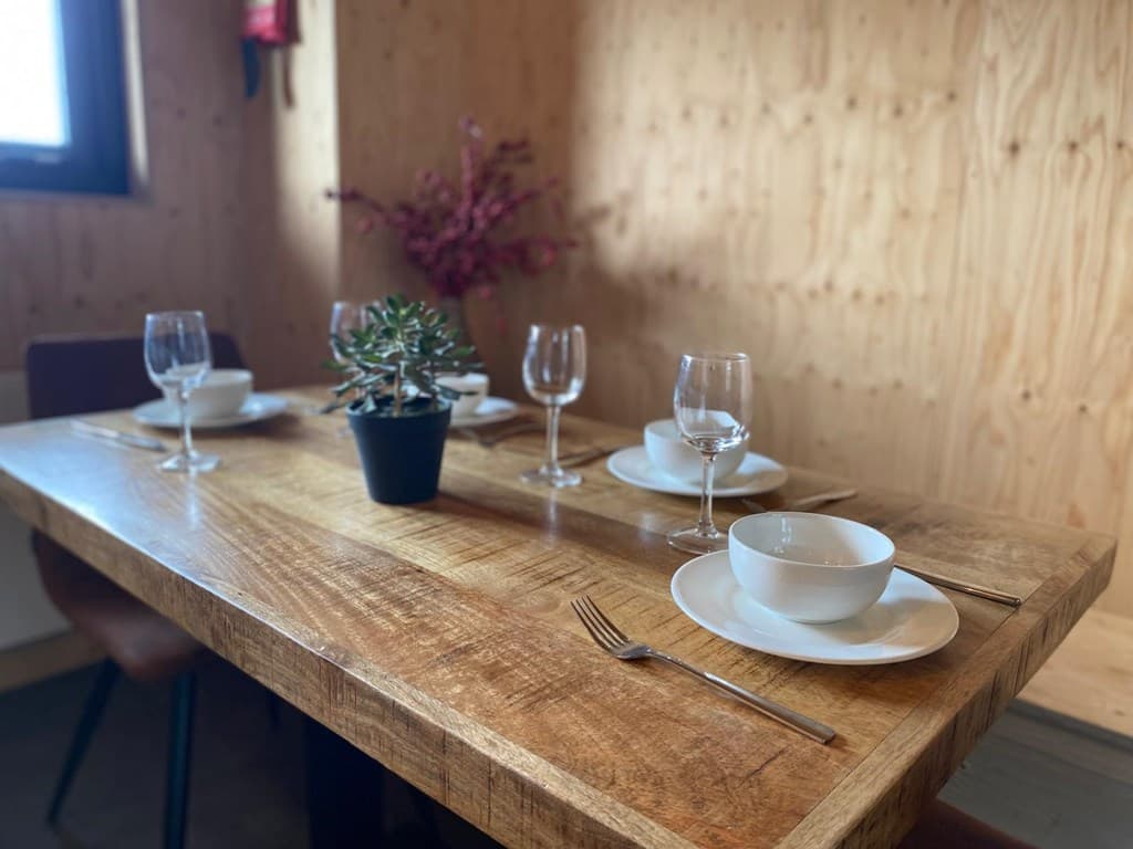 Eetruimte met houten tafel, glazen, borden en een plantje in een pot op de achtergrond met houten wand.