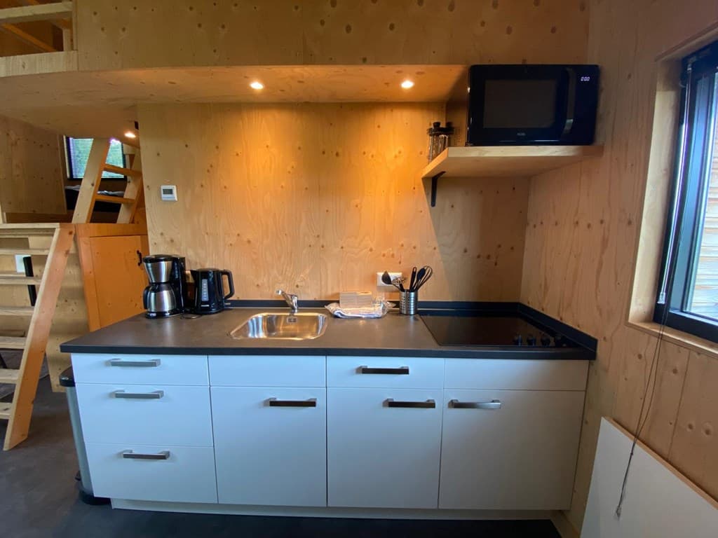 Keuken met een zwart aanrechtblad, metalen spoelbak, koffiezetapparaat en een magnetron aan de wand.