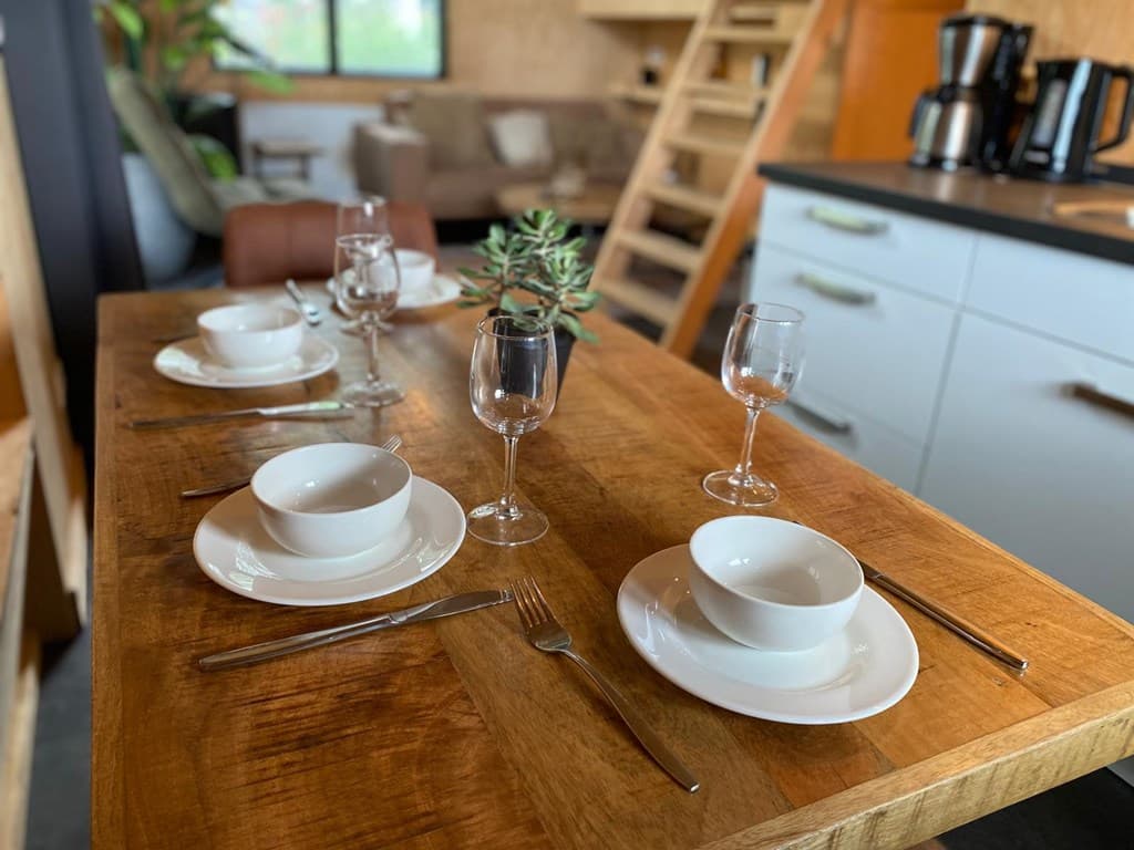 Eettafel met servies, glazen en bestek, in een moderne keuken met een gezellige zithoek op de achtergrond.