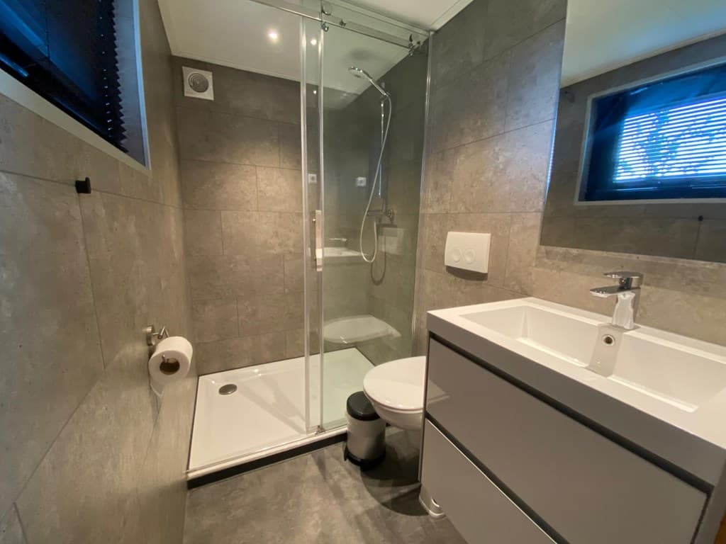 Moderne badkamer met douche, wastafel en toilet, betegelde wanden en vloeren in grijstinten.