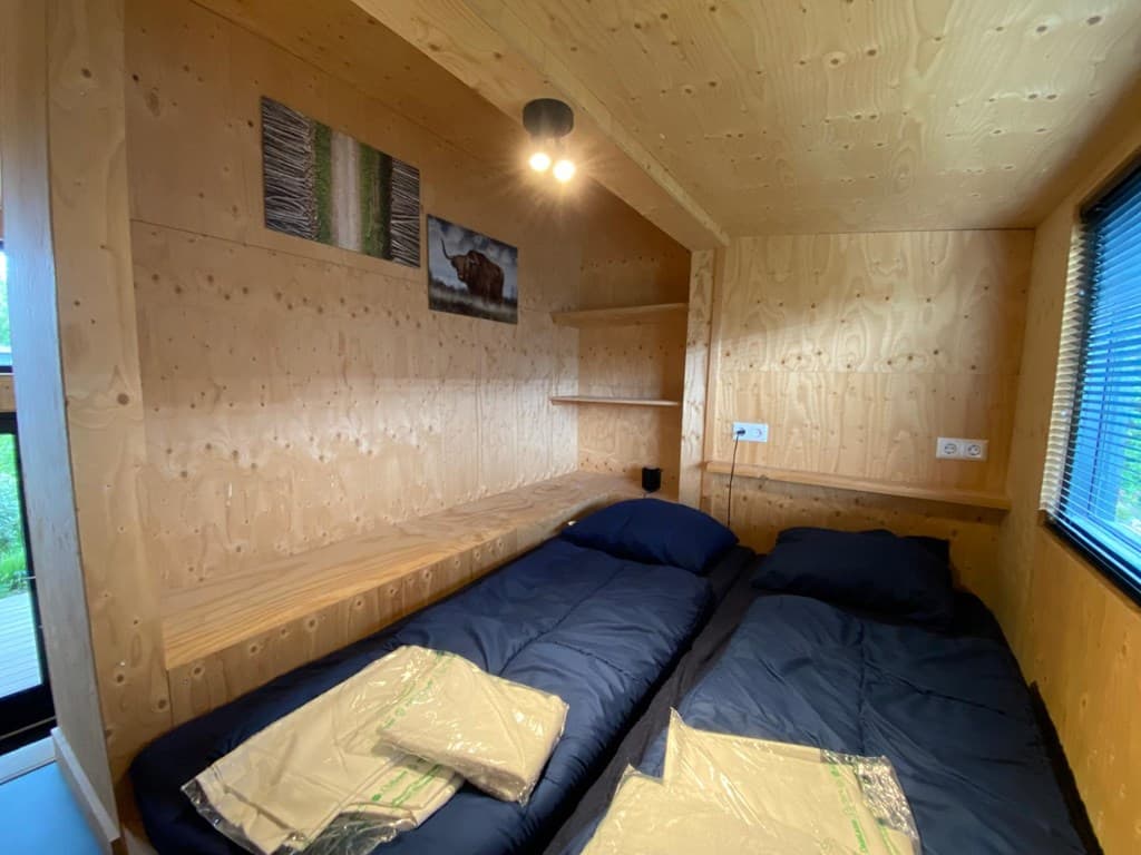 Slaapkamer met houten wanden, twee aparte bedden en verlichting aan het plafond.