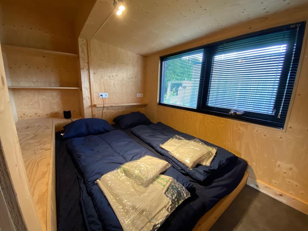 Slaapkamer met twee eenpersoonsbedden, houten wanden, en grote ramen met jaloezieën.