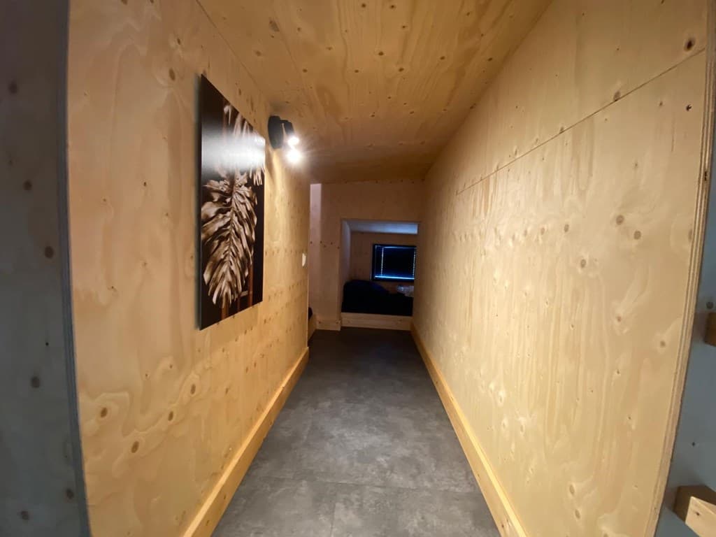 Lange gang met houten wanden en een stijlvol kunstwerk aan de muur, verlicht door een inbouwlamp