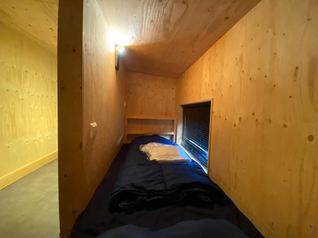Sfeervolle slaapkamer met houten wanden, een bed en een raam met jaloezieën.