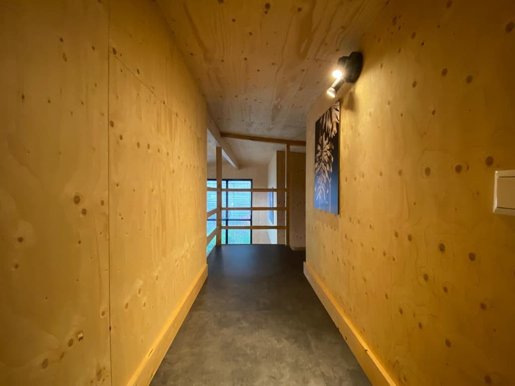 Gang met houten wanden en een raam dat uitzicht biedt op de buitenruimte, verlicht door een wandlamp
