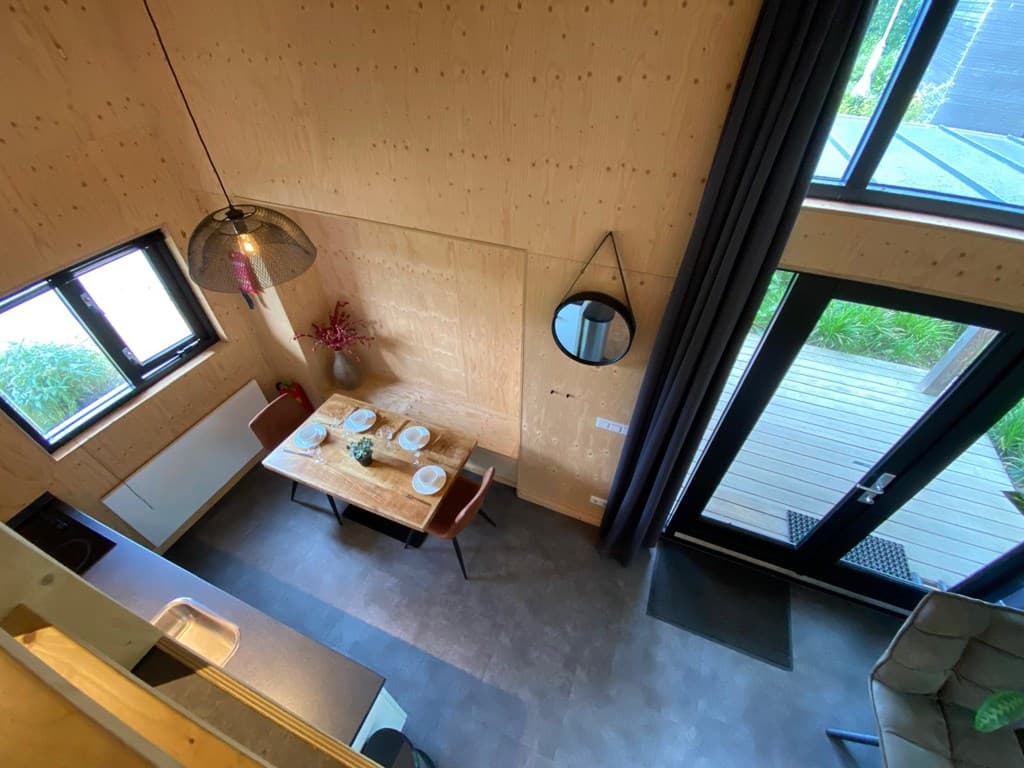 Zicht op de eethoek met tafel en stoelen, ramen bieden natuurlijk licht en toegang tot een terras buiten.