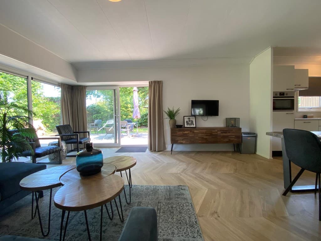 Moderne woonkamer met houten vloer, banken, salontafels, televisie en openslaande deuren naar de tuin