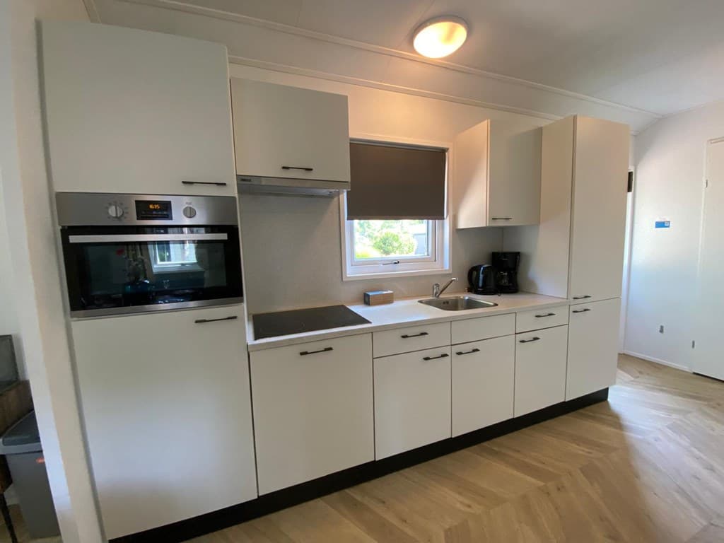 Moderne keuken met witte kasten, oven, kookplaat en koffiezetapparaat, gelegen in een woning.