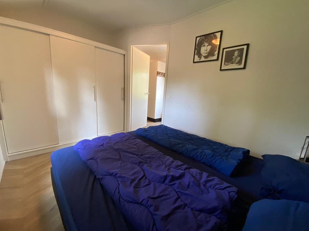 Slaapkamer met twee blauwe bedden, kast en twee zwart-wit foto's aan de muur. De deur opent naar een andere ruimte.
