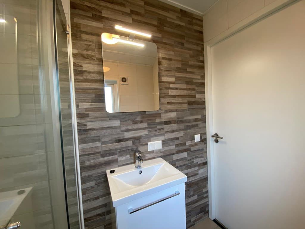 Badkamer met moderne wastafel, grote spiegel en eigentijdse wandbekleding van houtlook tegels.