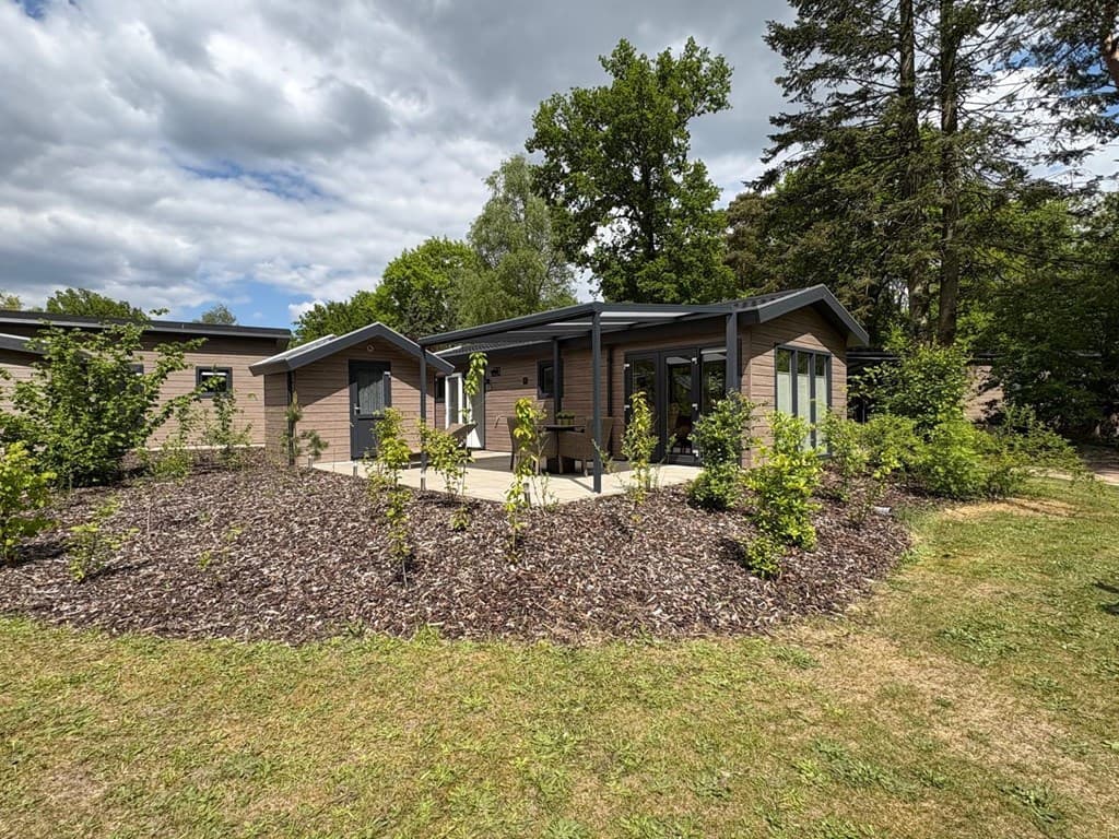 Moderne vakantiewoning omringd door groen, met een betegeld terras en grote ramen in een bosrijke omgeving.