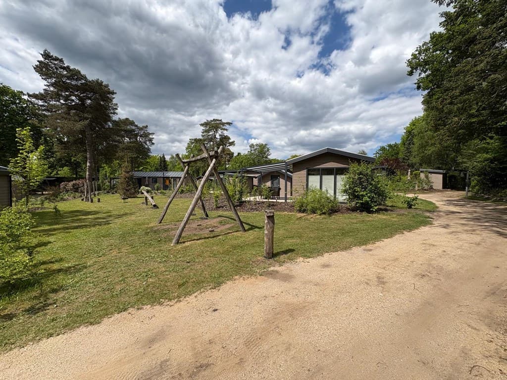 Vakantiewoning op Veluwepark de Bosgraaf met groene omgeving, speeltoestel en verhard pad in zandkleur.