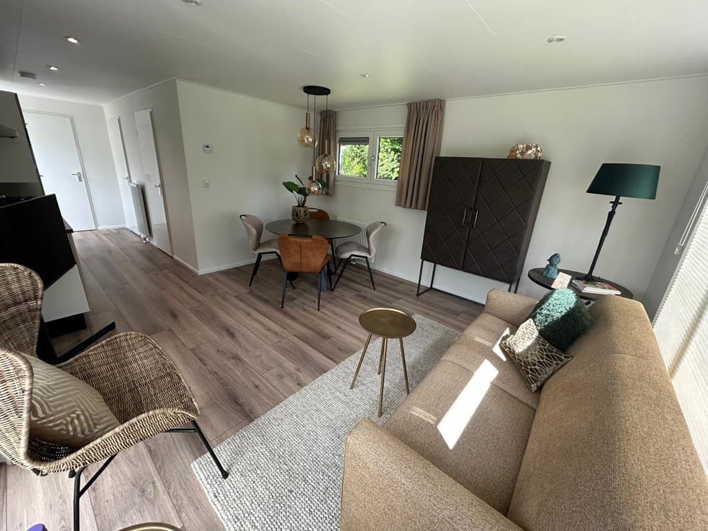 Moderne woonkamer met een zithoek, eettafel en kast, veel lichtinval en houten vloer