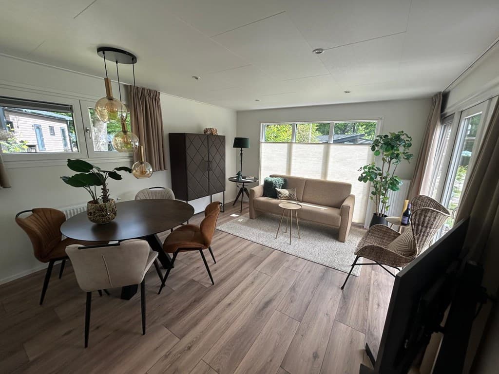 Ingerichte woonkamer met eettafel, zithoek en grote ramen voor natuurlijk licht en uitzicht op de tuin
