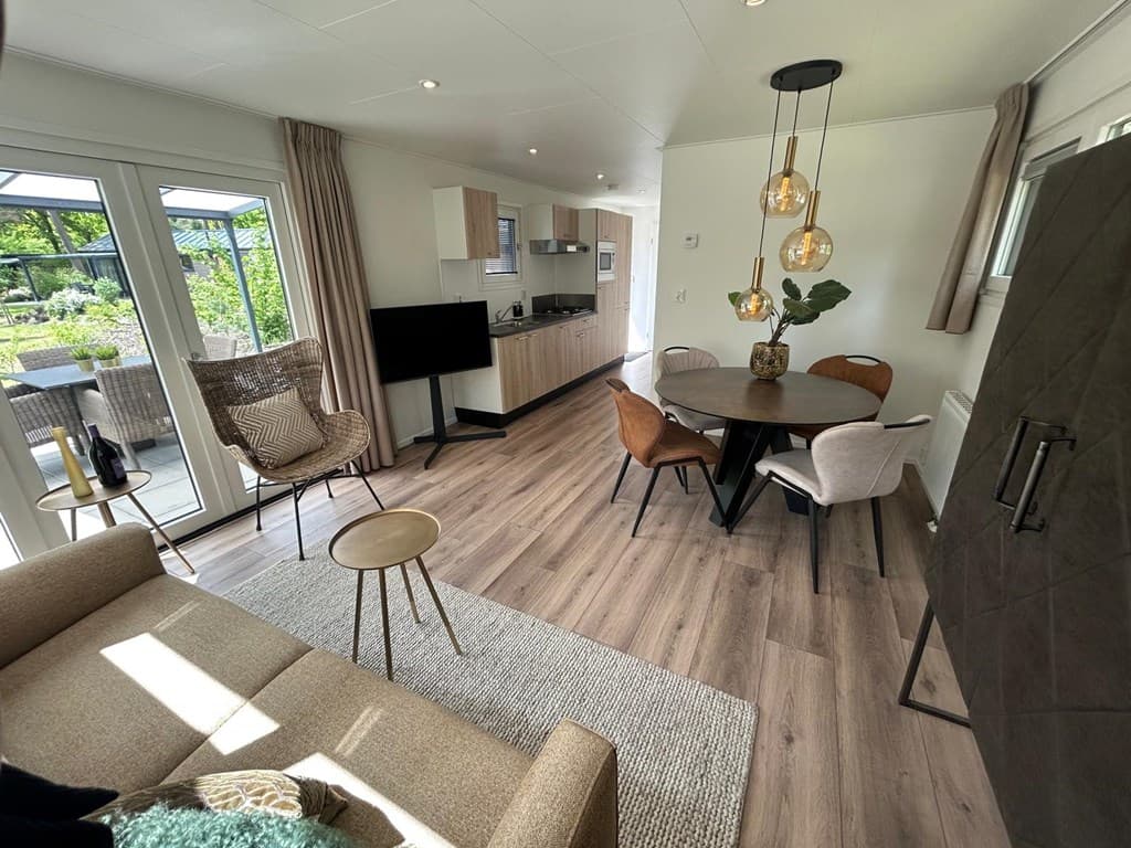 Moderne woonkamer met zithoek, open keuken en eettafel, grote ramen geven uitzicht op de tuin