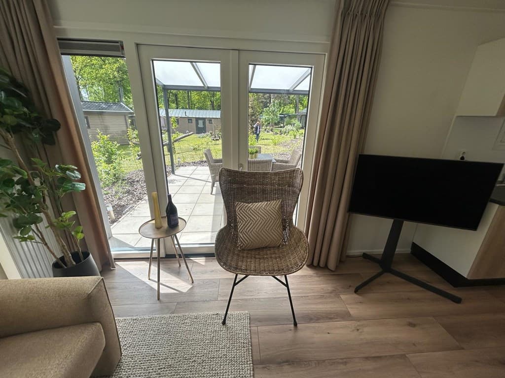 Zicht op een modern interieur met een zitzak, plant en glazen deuren naar een buitenruimte met terras en tuin.