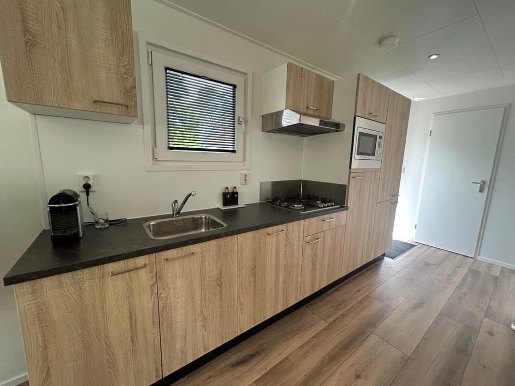 Moderne keuken met houtlook kasten, spoelbak, kookplaat en oven in lichte ruimte met venster en deur.