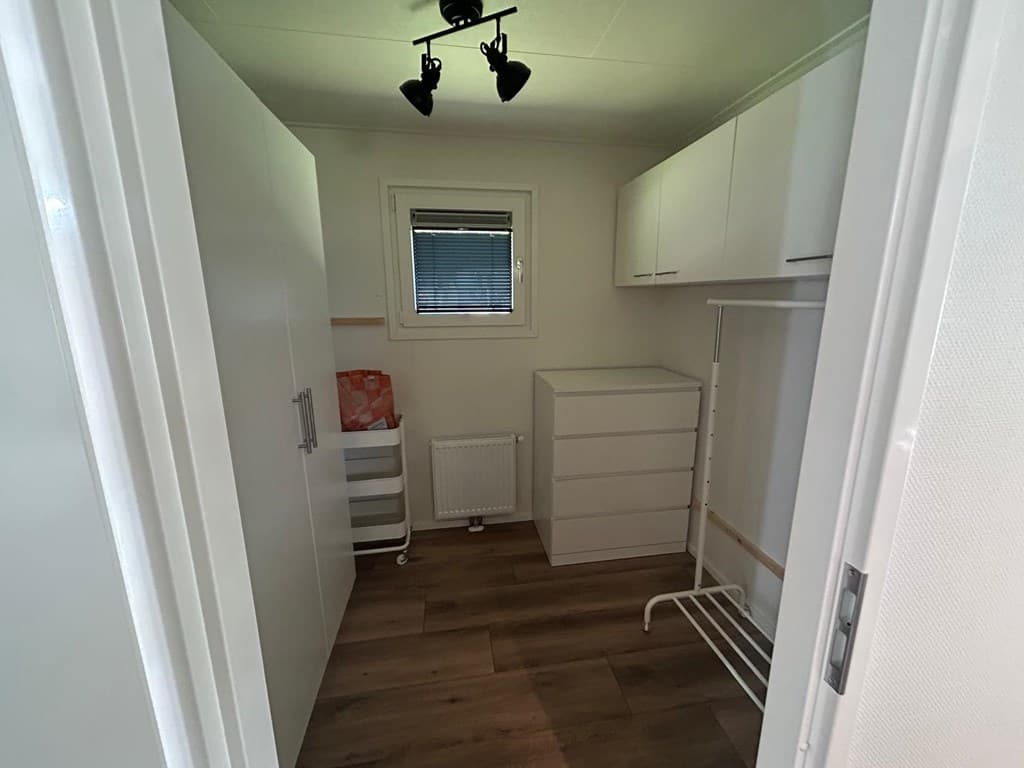 Inpandige berging met witte kasten, een ladekast en een raam voor natuurlijk licht.