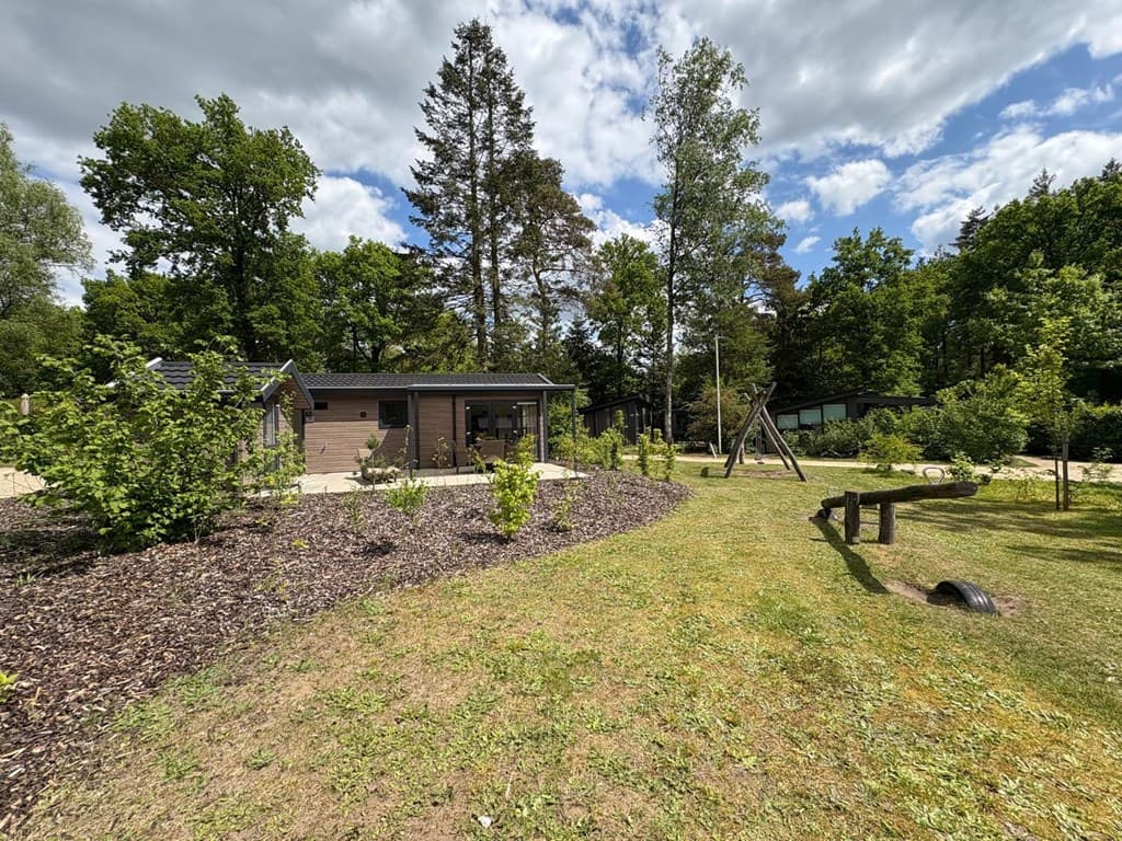 Vervolgde vakantiewoning met tuin, groene grasvelden, bomen en speeltoestel in een parkachtige omgeving.