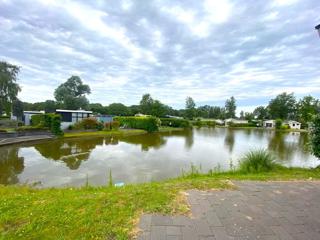 Uitzicht op het meer omringd door groene struiken en vakantiewoningen in EuroParcs Spaarnwoude.